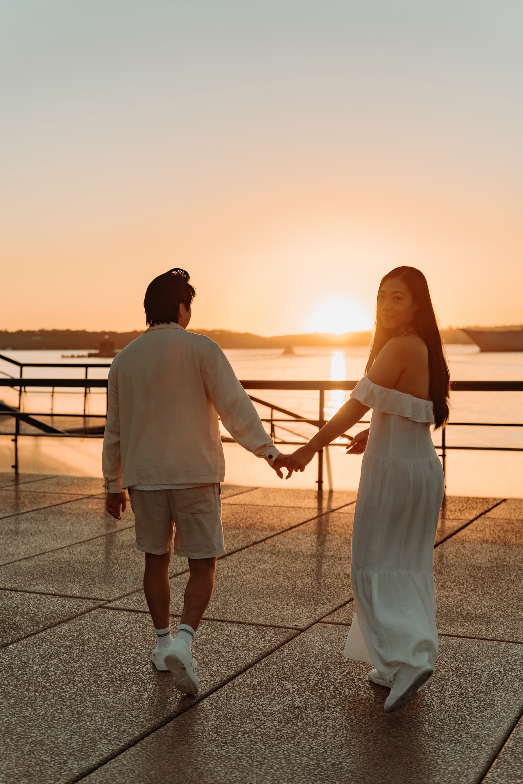 Stephanie and Terence walking hand in hand along the harbour at sunset